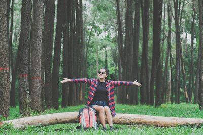 Full length of young woman sitting on tree trunk in forest