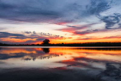 Scenic view of lake against dramatic sky during sunset