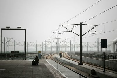 Power lines over railroad tracks against cloudy sky