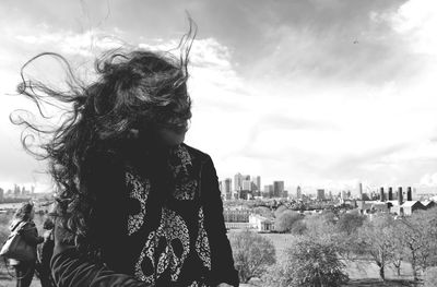 Woman with tousled hair against sky on windy day in city