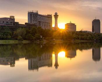 Scenic view of lake by buildings against sky during sunset