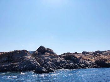 Rock formations by sea against clear blue sky