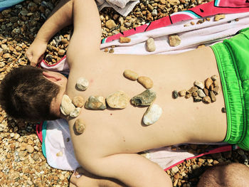 Rear view of shirtless man with stones on back lying at beach