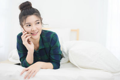 Smiling young woman holding phone on bed