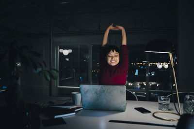 Smiling young businesswoman stretching while working late in coworking space