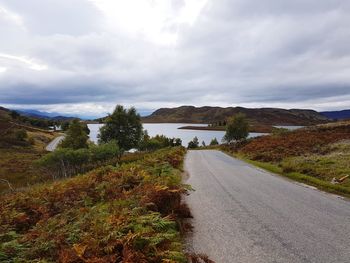 Road passing through landscape against cloudy sky