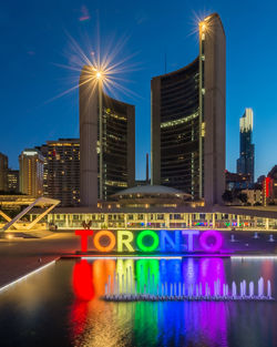 Illuminated city by river against sky at night