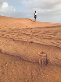 Rear view of man walking on desert against sky