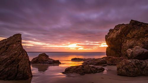 Rock formation by sea against sky during sunset