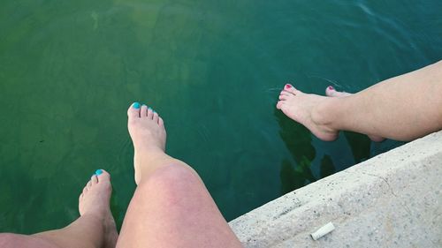 Low section of women sitting on pier over lake