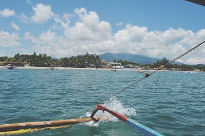 Cropped image of outrigger canoe sailing in sea against sky