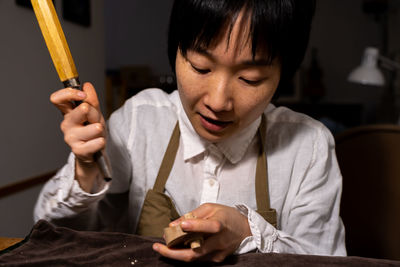 Young chinese female violin maker working with gouge to making a new violin in her workshop