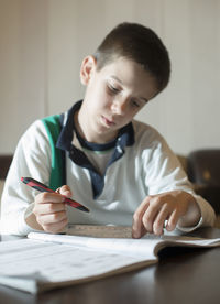 Boy writing in book while sitting on table