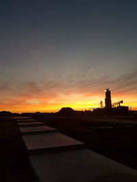 Silhouette of lighthouse against cloudy sky during sunset