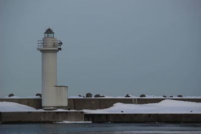 Lighthouse by sea against clear sky