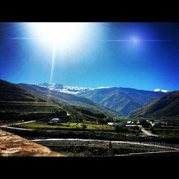 mountain, landscape, mountain range, tranquil scene, scenics, tranquility, beauty in nature, blue, road, sky, nature, sun, lens flare, sunlight, transfer print, transportation, sunbeam, non-urban scene, country road, clear sky