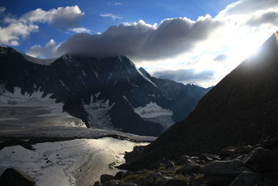 Glacier and mountains in the clouds with bright sun at sunset