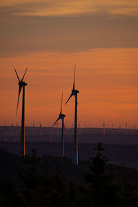 Silhouette wind turbines on land against sky