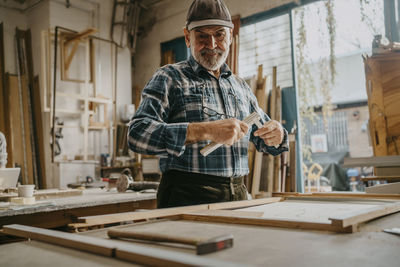 Focused senior male carpenter holding measuring tape at workshop