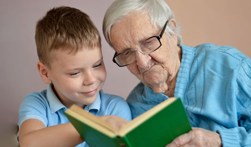 Portrait of white-hair eldery woman 90 years old with hergrandson at home, reading book together