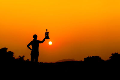 Silhouette woman holding trophy while standing on land against sky during sunset