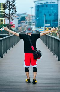 Rear view of man standing on footbridge in city