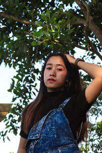 Low angle portrait of young woman standing against tree