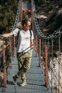 A man with a backpack on a suspension bridge against the backdrop of a mountain landscape with trees