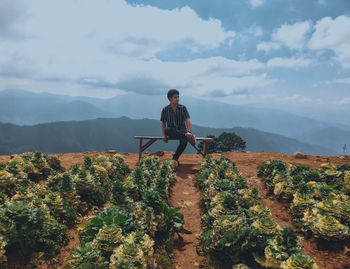 Man sitting by mountain against sky