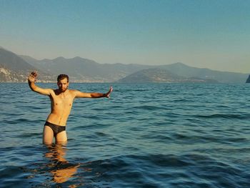 Full length of shirtless man in sea against clear sky