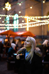 Young woman having drink at outdoor cafe in city at night