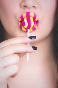 Cropped image of woman with yellow and pink lipstick eating lollipop