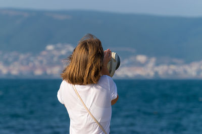 Rear view of woman looking at sea through coin-operated binoculars against sky