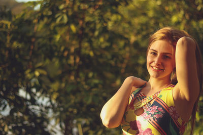 Portrait of smiling young woman posing against trees at park