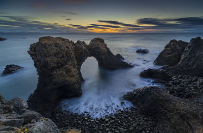 Rocks in sea against sky during sunset