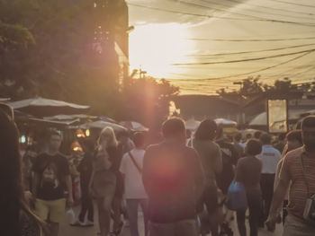 Rear view of people walking on street in city at sunset