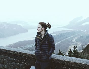 Young man standing against mountain and river during winter
