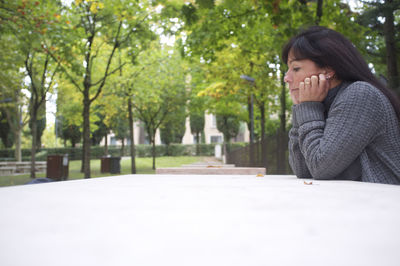 Side view of young woman looking away against trees