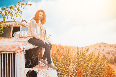 Portrait of smiling young woman sitting against sky