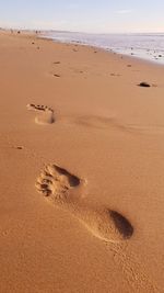 Footprints on sand at beach against sky