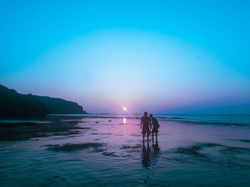 Men on beach against sky during sunset