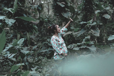 Side view of pregnant woman standing by trees in forest