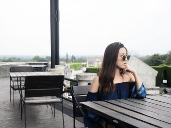 Young woman sitting at outdoor cafe against clear sky