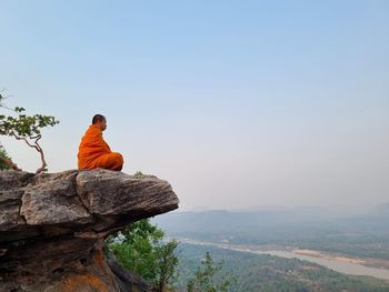 Rear view of woman sitting on rock against clear sky