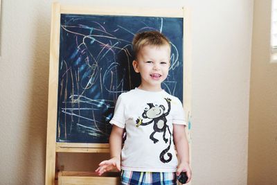 Portrait of smiling cute boy standing against blackboard