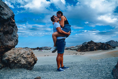 Young man standing on rock against sky