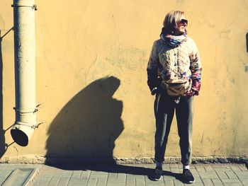 Full length of woman standing on footpath against wall