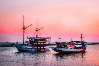 Sailboats moored on sea against sky during sunset