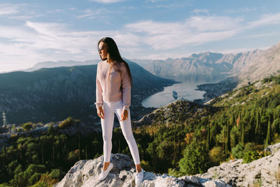 Full length of young woman standing on rock against sky