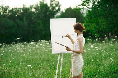 Woman holding umbrella standing on field against trees